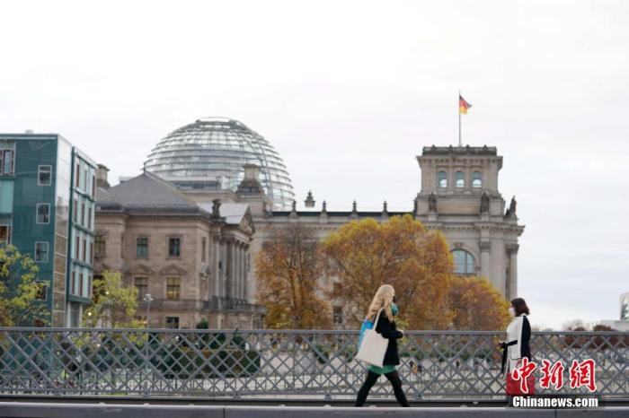 资料图：两名戴口罩的女士从德国国会大厦旁的桥上经过。中新社记者 彭大伟 摄