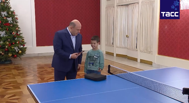 俄总理米舒斯京向10岁小男孩展示乒乓球拍的画面。图源：塔斯社视频截图