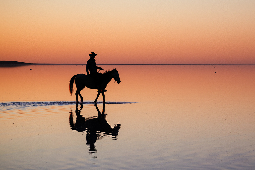 土耳其骑手落日余晖中策马奔腾微波水面留下完美倒影