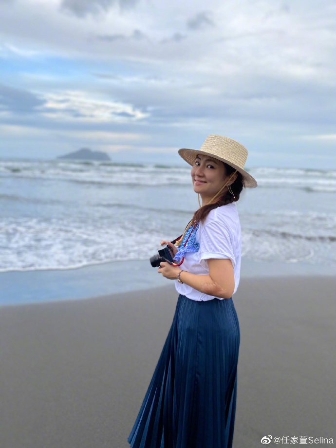 照片中,selina头戴草帽,编麻花辫,身穿白色t恤搭配牛仔长裙,休闲惬意.