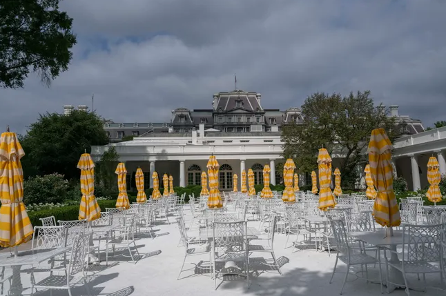 当地时间8月16日，白宫玫瑰园里的白色金属桌椅和黄色遮阳伞。图源：美媒