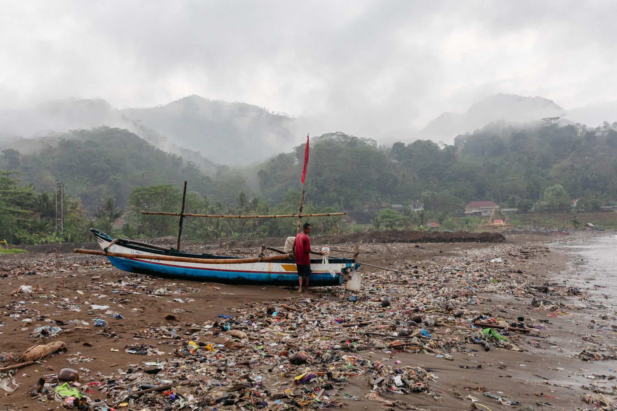 印度尼西亚西爪哇省罗吉海滩上，当地渔民正在维护船只，周围都是被冲上来的垃圾。图源：CNN