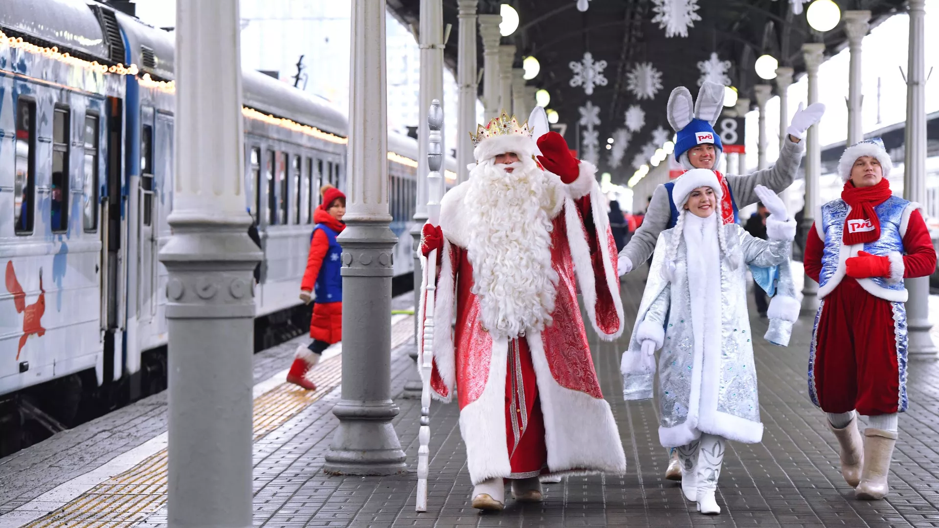 俄新社称，这是2023年新年前夕俄罗斯装扮成“严寒老人”和“雪姑娘”的人员招手的画面。
