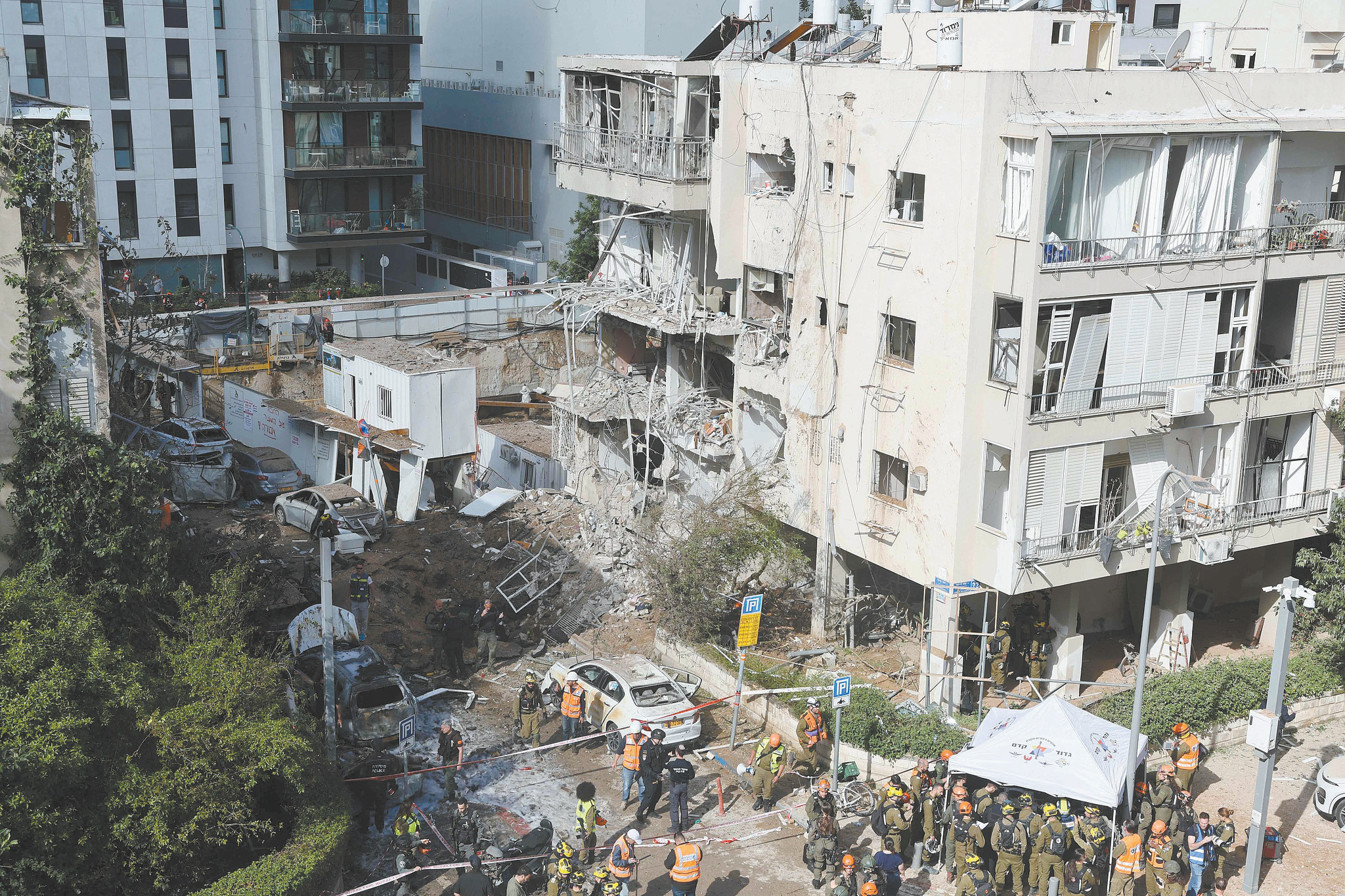 当地时间24日，以色列应急救援人员聚集在特拉维夫一处遭伊朗导弹袭击的现场。（视觉中国）