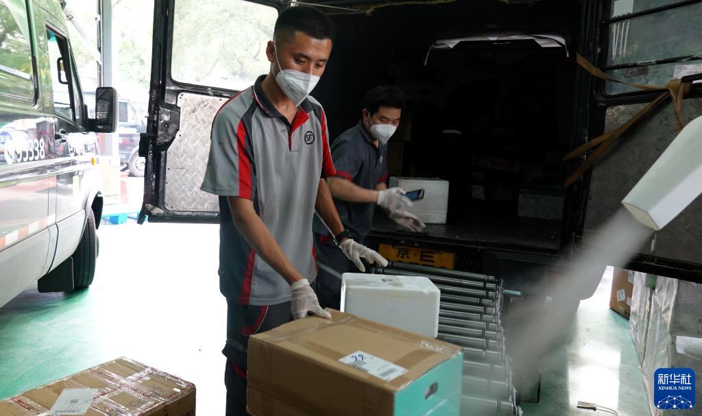 在北京市西城区陶然亭街道一处顺丰速运营业点，刘阔（左）和同事用传送带卸货并进行外包装消毒（2022年6月25日摄）。新华社记者 陈旭 摄