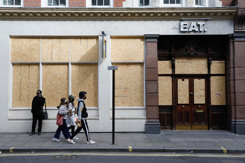 3月21日，在英国伦敦，人们戴着口罩从一家关闭的餐馆前走过。新华社发（蒂姆·爱尔兰摄）