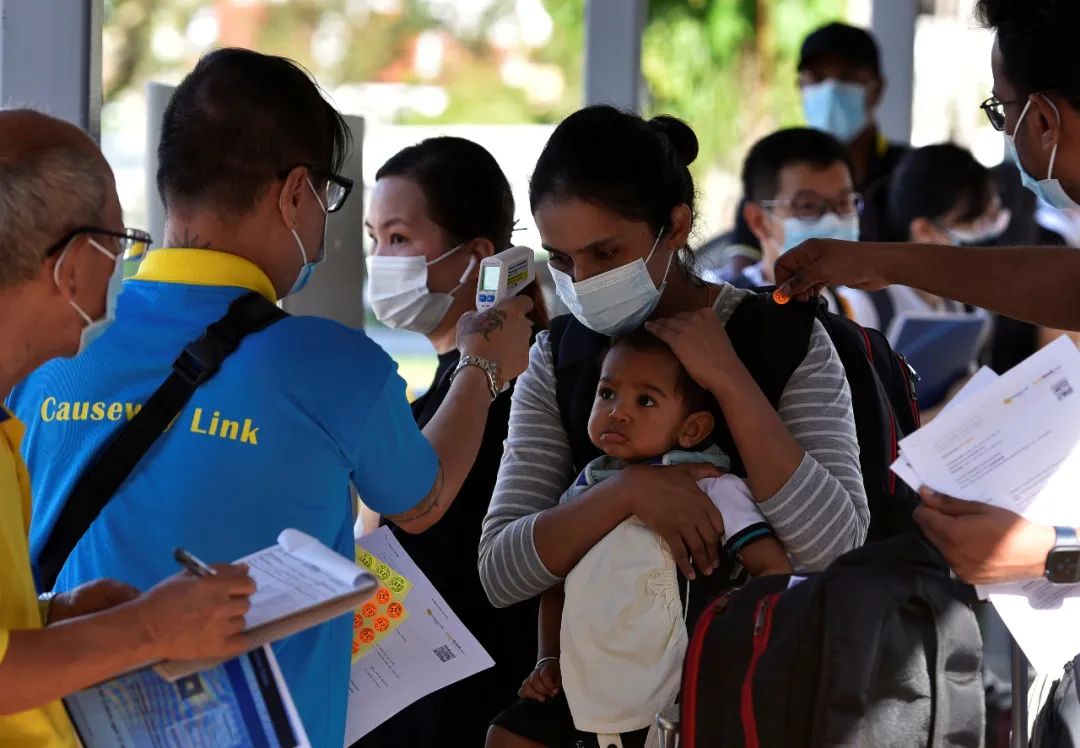 ▲ 2021年11月29日，一位母亲和孩童正在新加坡公交车站接受体温检查，随后乘坐公共汽车回到马来西亚。此前，新马两国边境关闭了近两年。