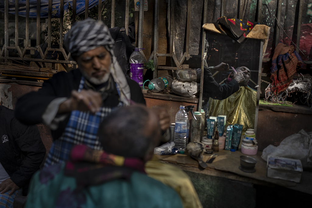 当地时间2023年12月20日,印度新德里,老人在理发店为顾客理发.