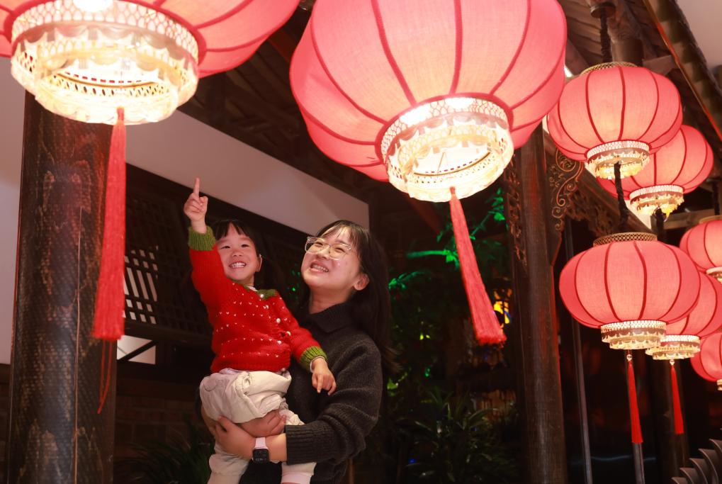 2月14日，人们在湖北省武汉市武昌区一家购物中心红灯笼下玩耍。新华社发（赵军 摄）